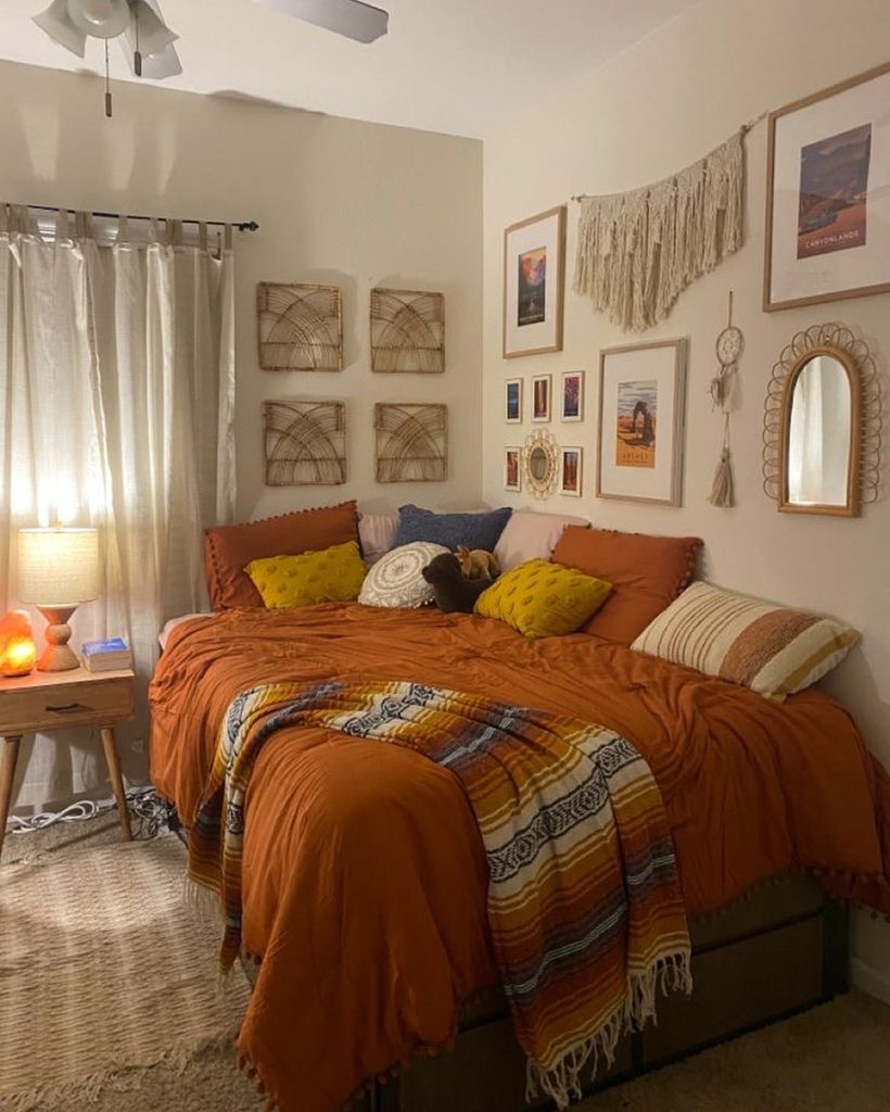 Rustic bedroom with warm rust bedding, macrame wall decor, and soft lighting.