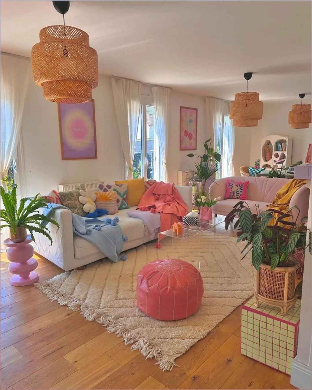 Soft pastel living room with pink pouf, neutral rug, and airy curtains.
