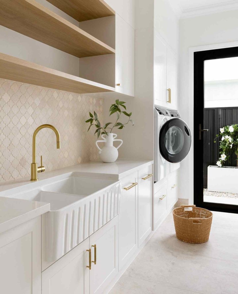 Bright laundry room with a farmhouse sink, gold fixtures, and patterned tile floor.
