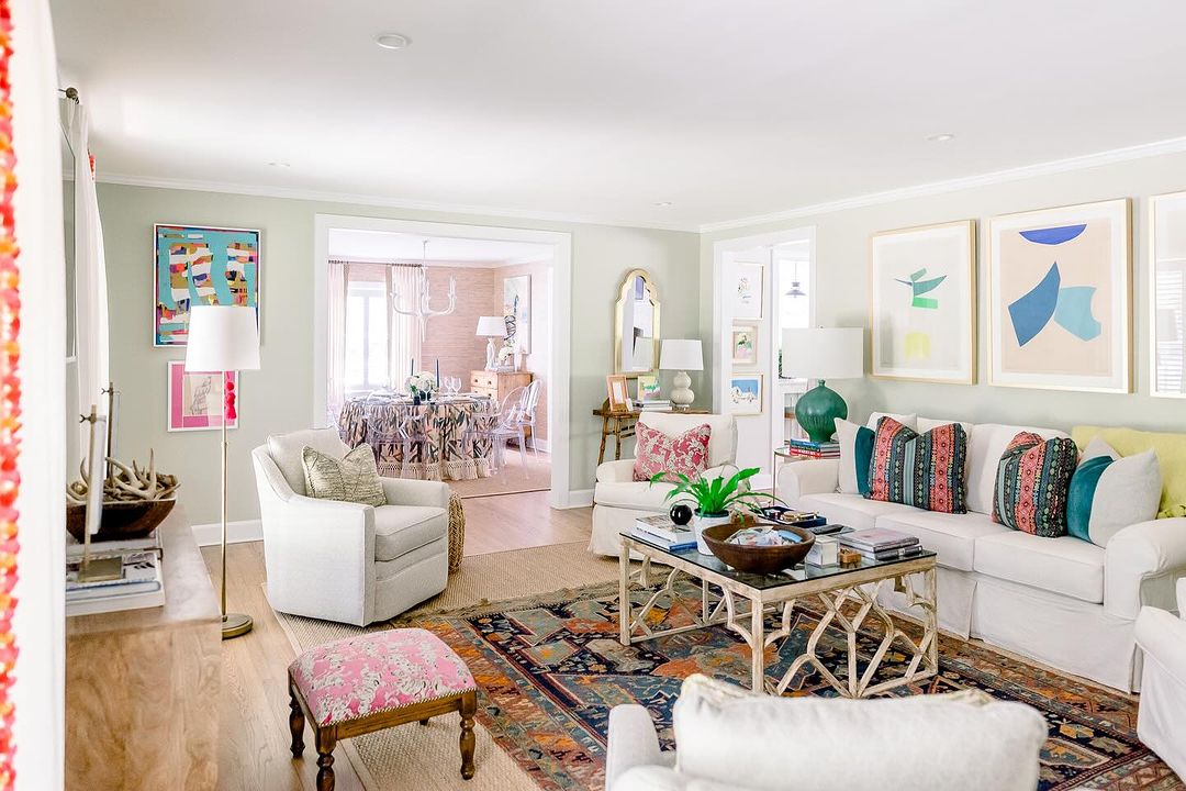 Subtle green living room with colorful patterned pillows and vibrant rug.
