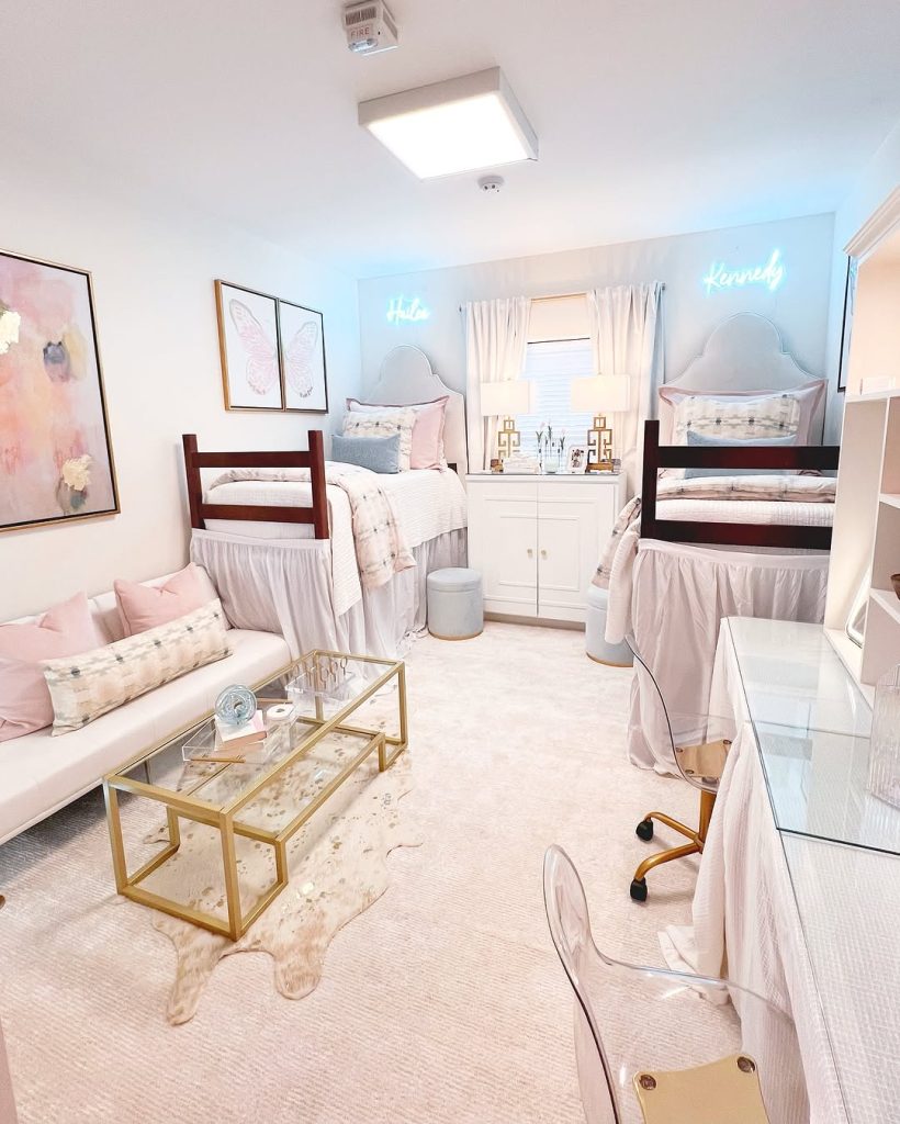 Chic dorm with blush and gold accents, a seating area, and a glass coffee table.
