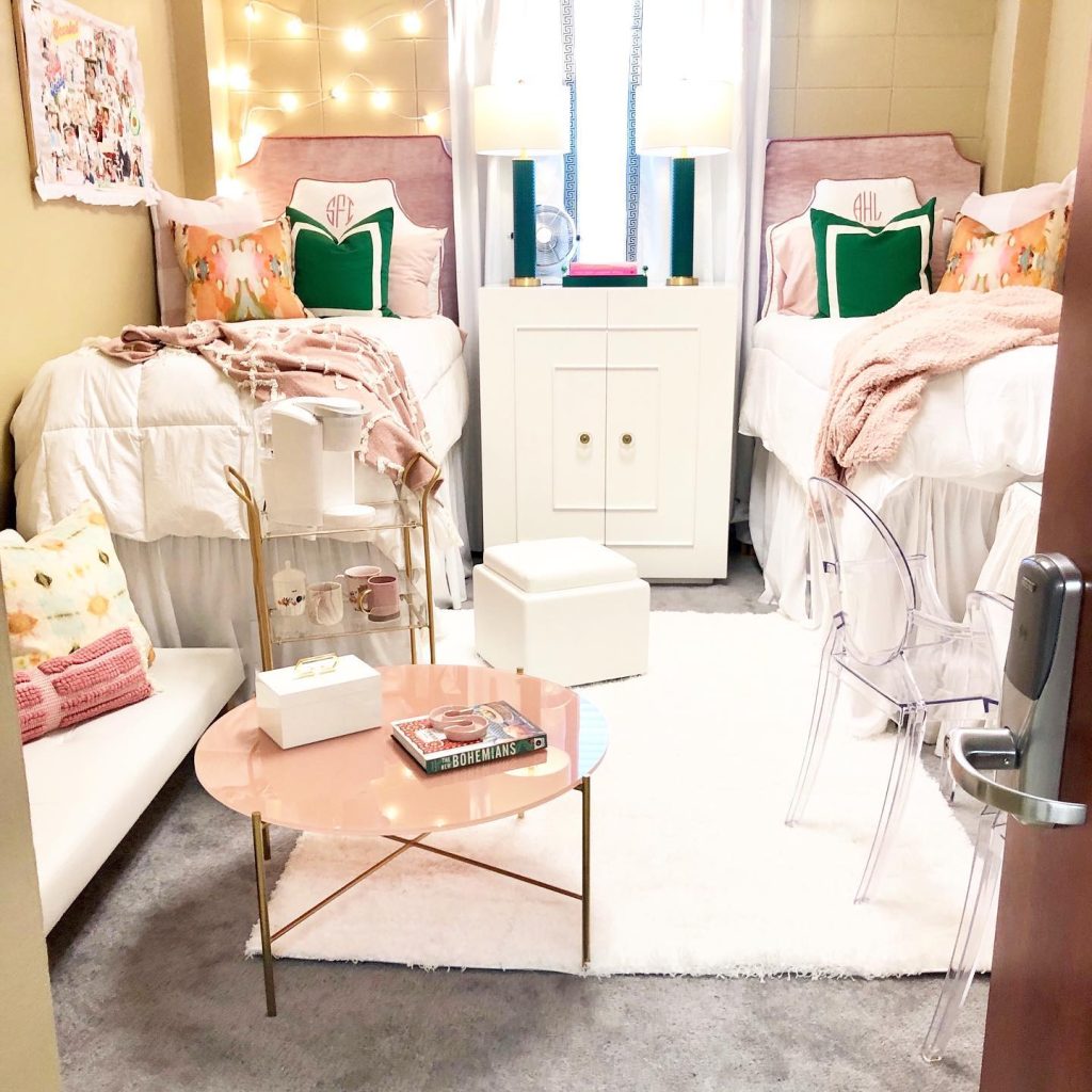 Modern dorm with monogrammed pillows, pastel tones, and a rose gold coffee table.
