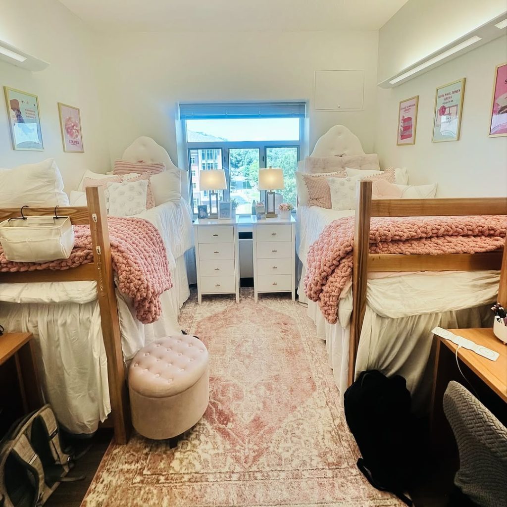 Blush-toned dorm with chunky knit blankets, tufted ottoman, and a symmetrical design.
