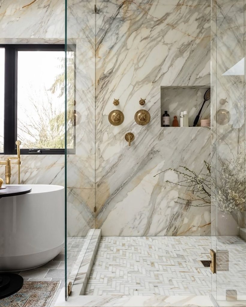 Golden-veined marble shower with herringbone flooring and natural light