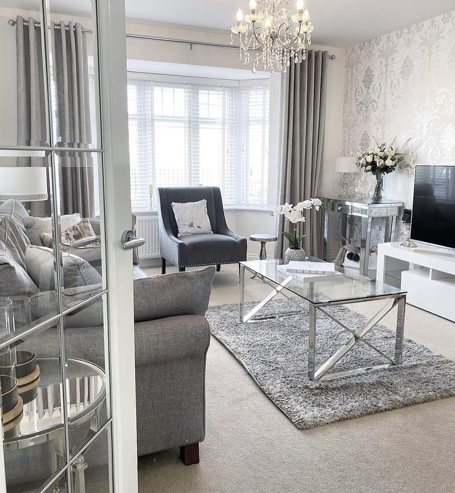 Elegant grey living room with a crystal chandelier and mirrored decor.
