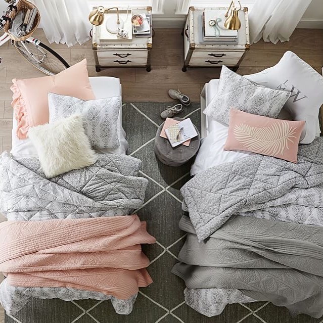 Balanced dorm with soft pink and gray bedding, vintage nightstands, and brass accents.
