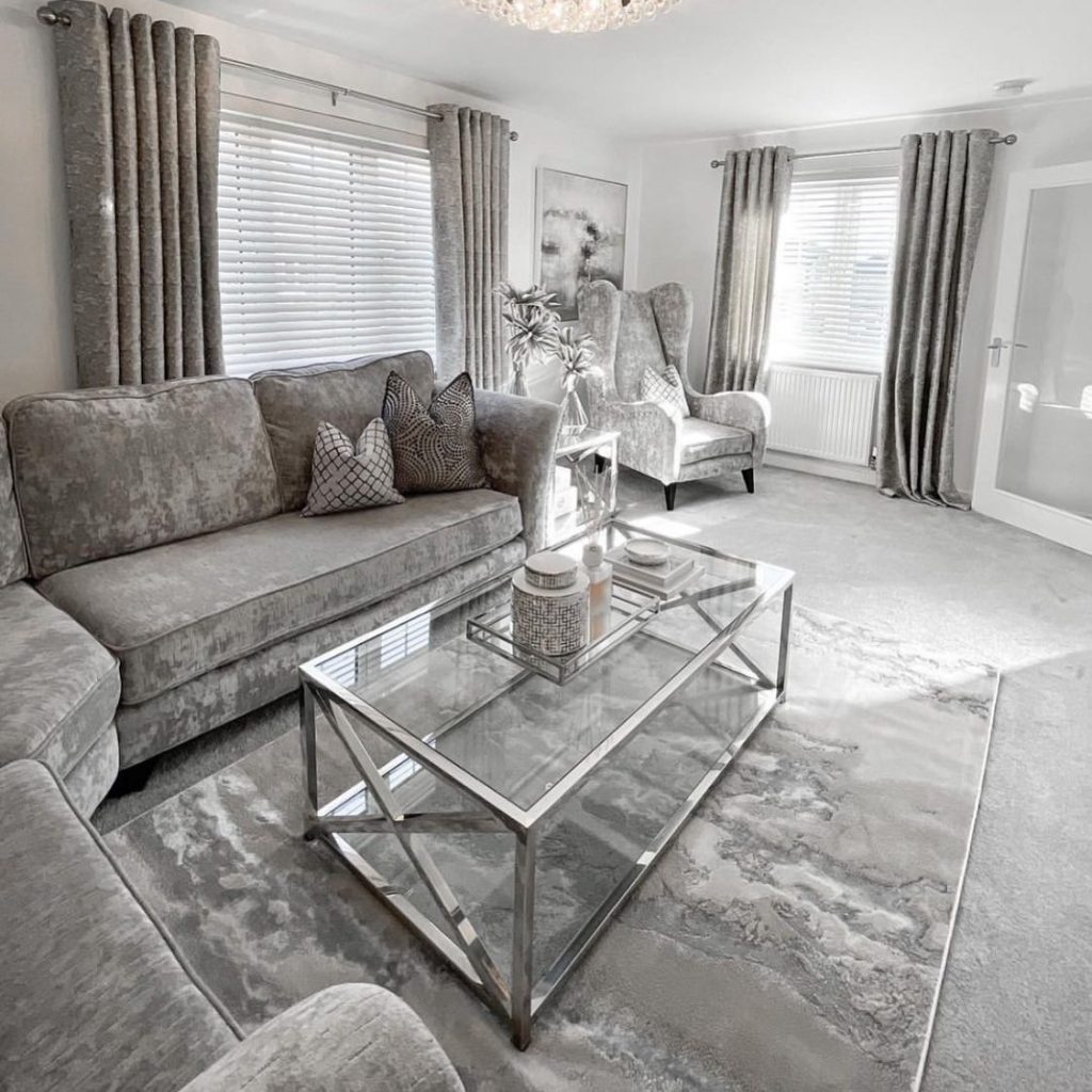 Velvet grey living room with a glass coffee table and soft lighting.
