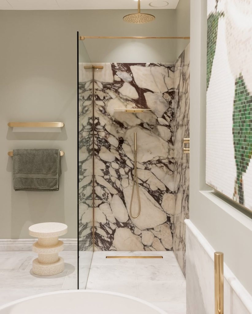 Dark veined marble shower balanced with soft sage walls and gold accents.