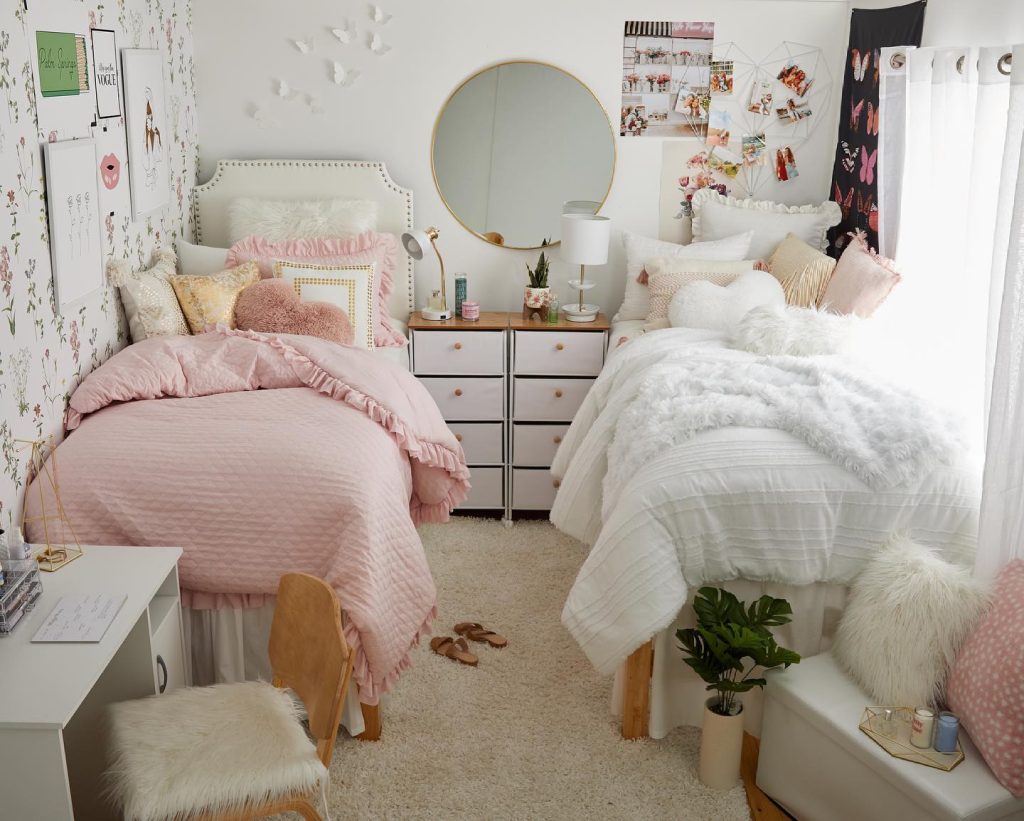 Pastel-themed dorm with a round mirror, pink and white bedding, and a stylish gallery wall.
