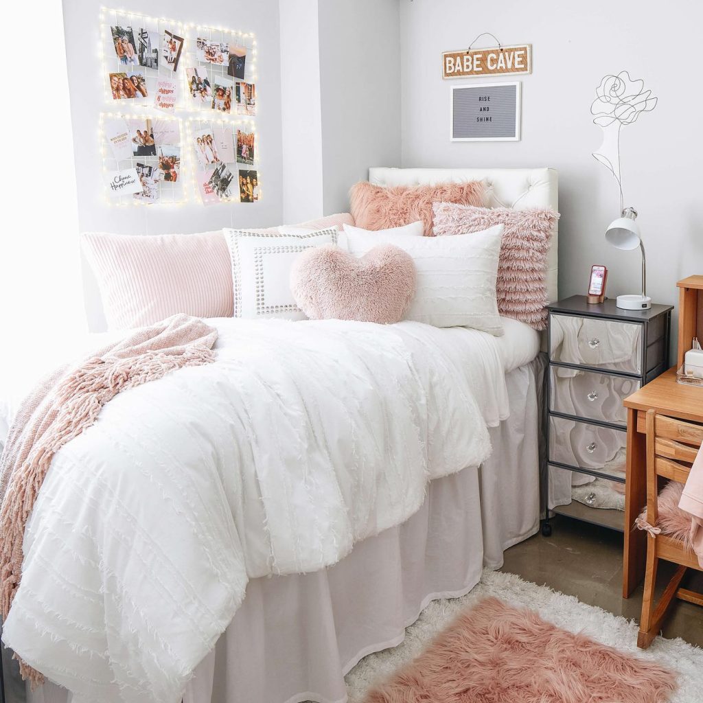 Soft and sweet dorm setup with pink pillows, a heart-shaped pillow, and twinkling photo string lights.
