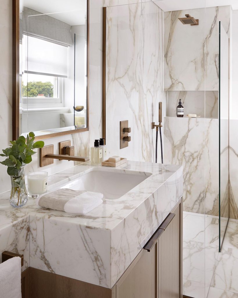 Creamy marble bathroom with brass fixtures and wood cabinetry