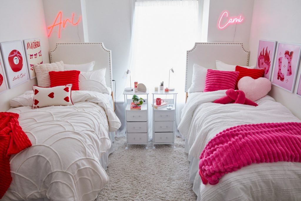 Coordinated dorm with bold red and pink accents, matching white bedding, and personalized neon names.
