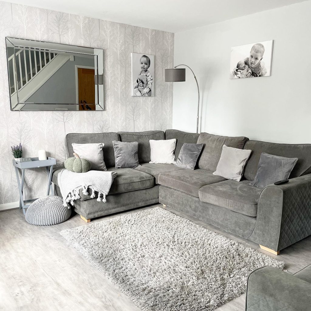 Spacious grey sectional with tree-patterned wallpaper and personal photos.
