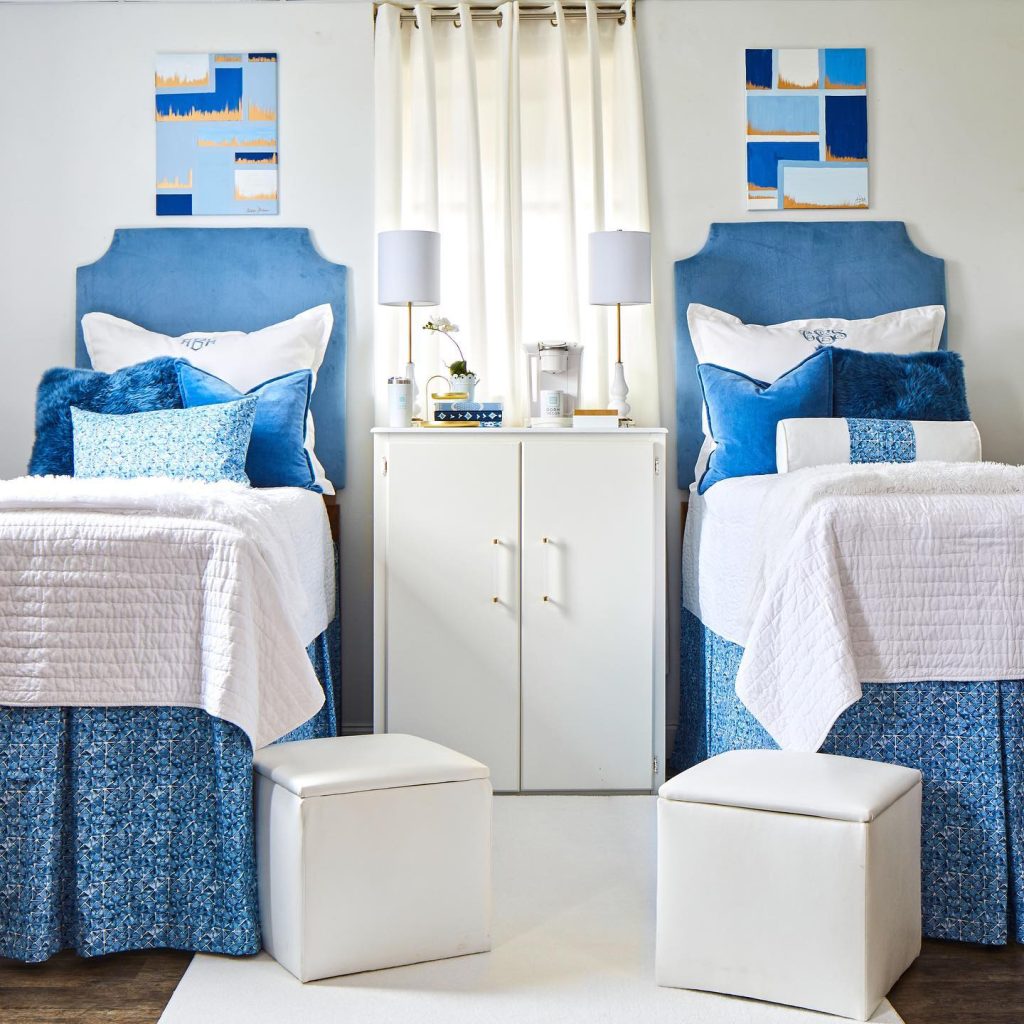 Sophisticated dorm with blue accents, plush headboards, and storage ottomans in a symmetrical layout.
