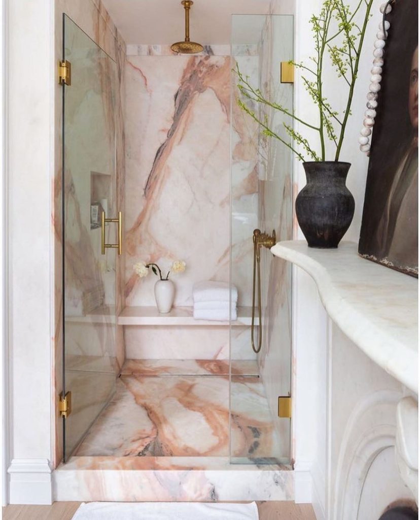 Blush-toned marble shower with brass fixtures and soft lighting