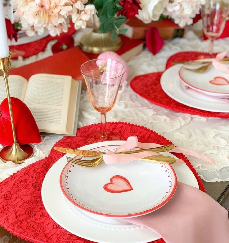 Heart-themed romantic table setting for two with red lace accents and floral centerpiece.
