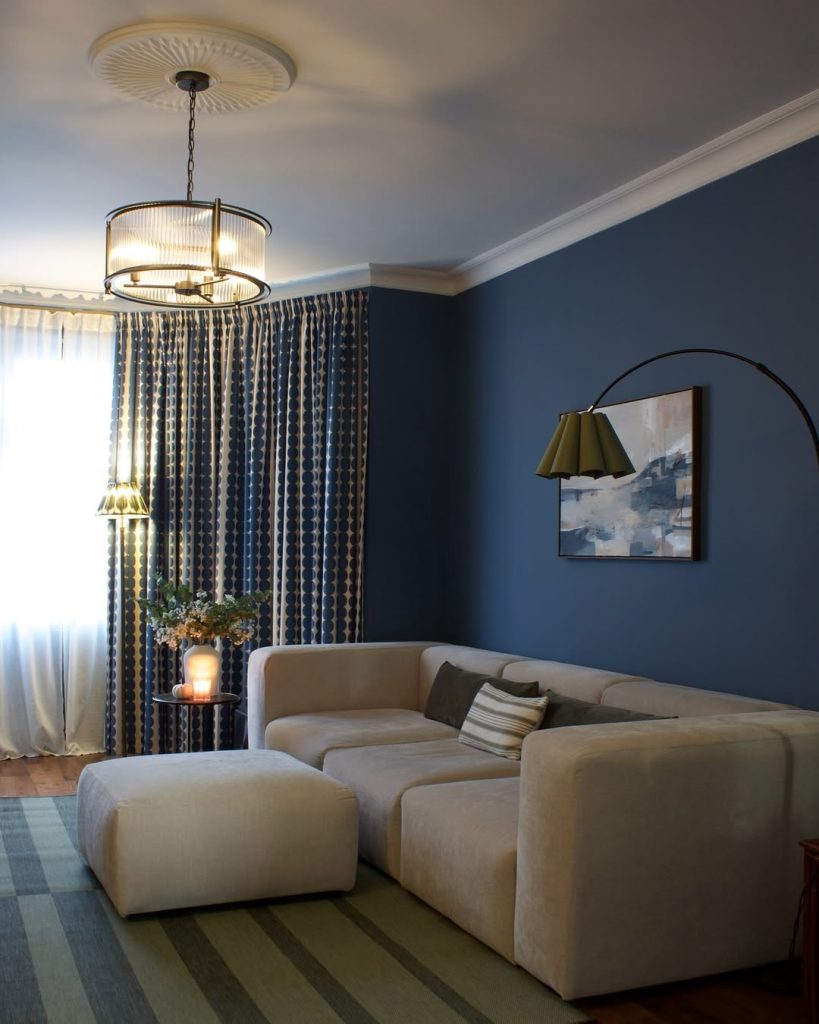 Navy blue walls with cozy beige furniture and modern lighting in a chic living room.