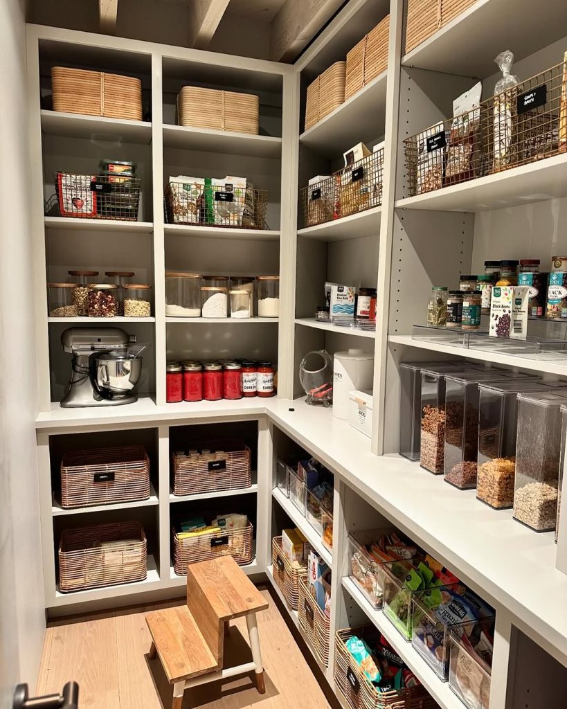 Walk-in pantry with wooden baskets, metal storage bins, and a step stool.
