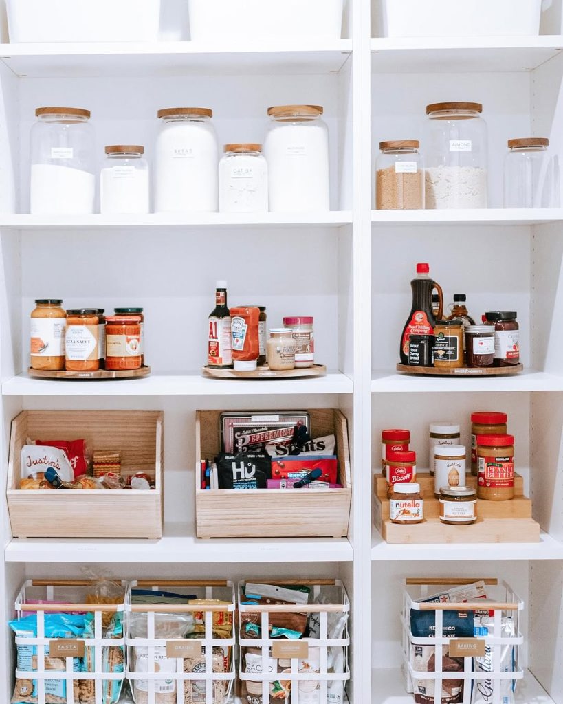 Crisp and clean pantry with labeled jars, wooden bins, and wire baskets.
