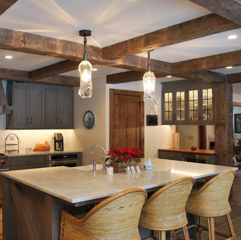 Warm cozy kitchen with exposed wooden beams, rattan bar stools, and rustic decor.
