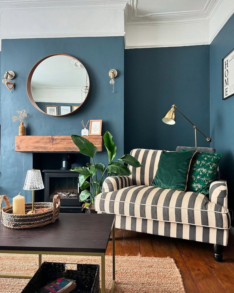 Dark blue walls with a striped loveseat and a warm wood mantel for classic charm