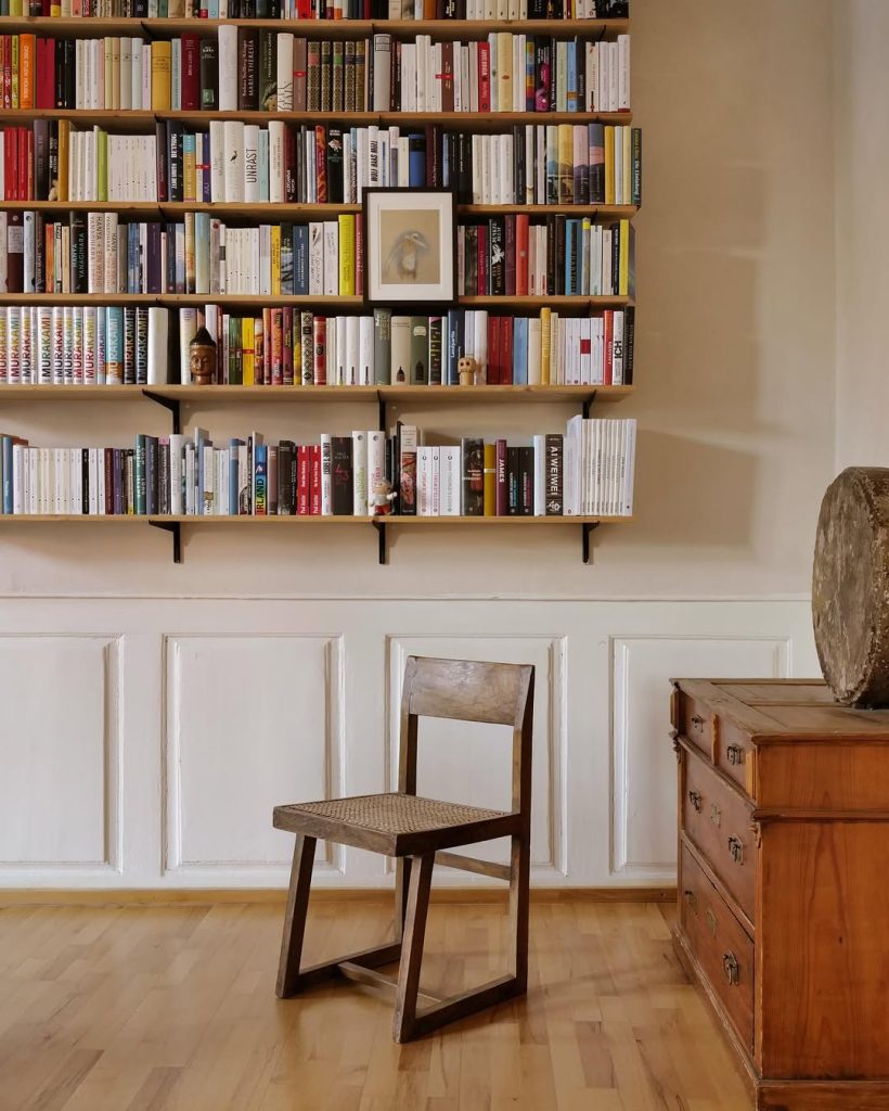 A chair positioned in front of a bookshelf filled with numerous books, creating a cozy reading nook.