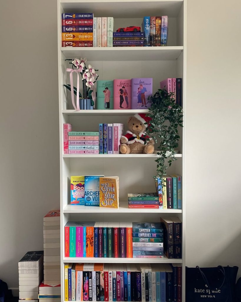 A cozy bookshelf filled with various books alongside a cute teddy bear resting on the shelf.