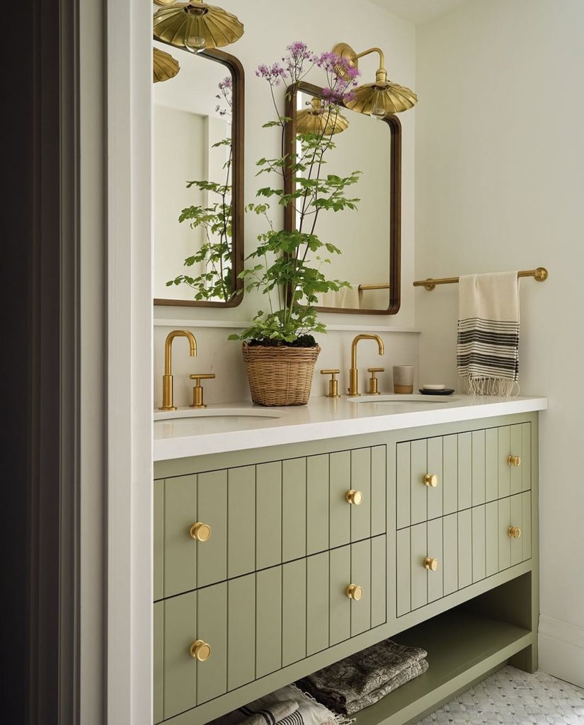 Nature-inspired double sink bathroom with sage green vanity and brass finishes.
