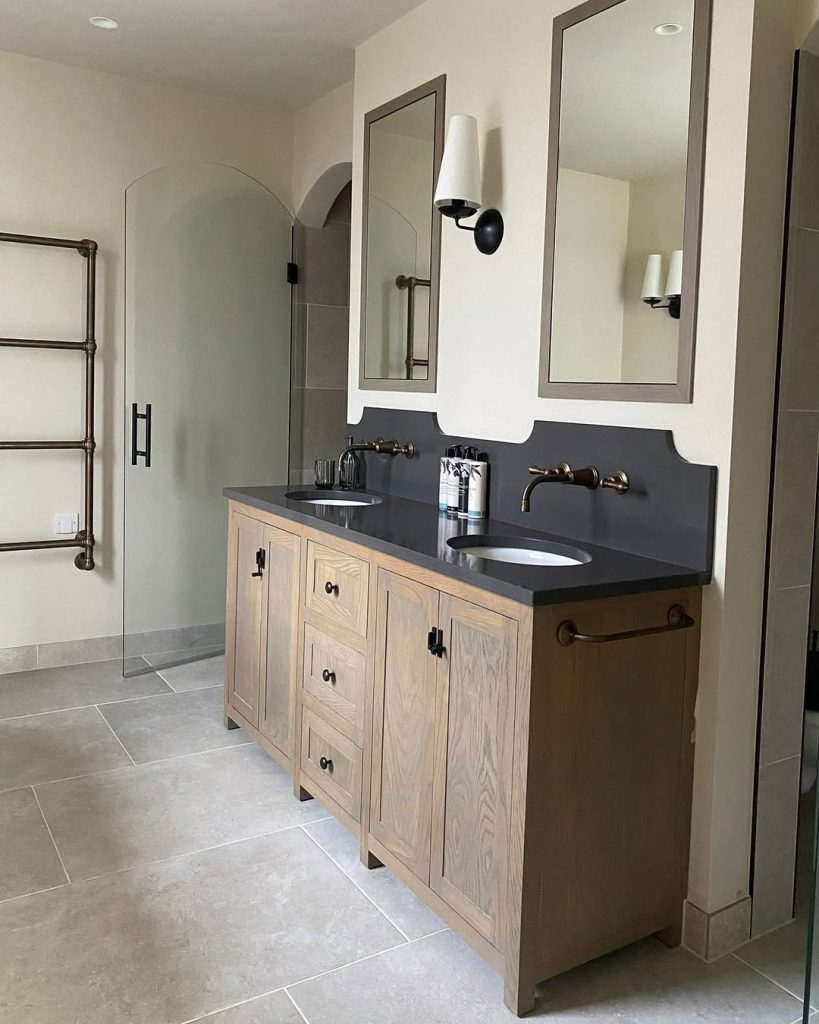 Rustic-meets-modern double vanity bathroom with dark countertops and wood cabinets.
