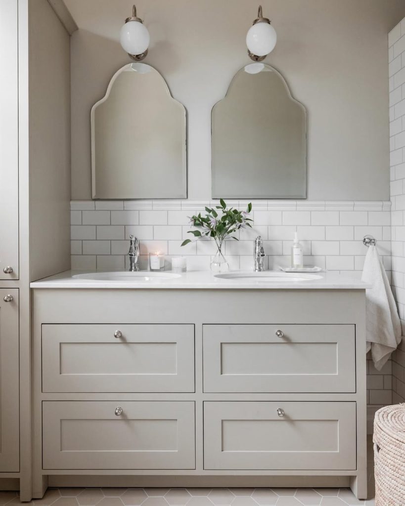 Light and airy modern double vanity bathroom with glass shower and gold fixtures.
