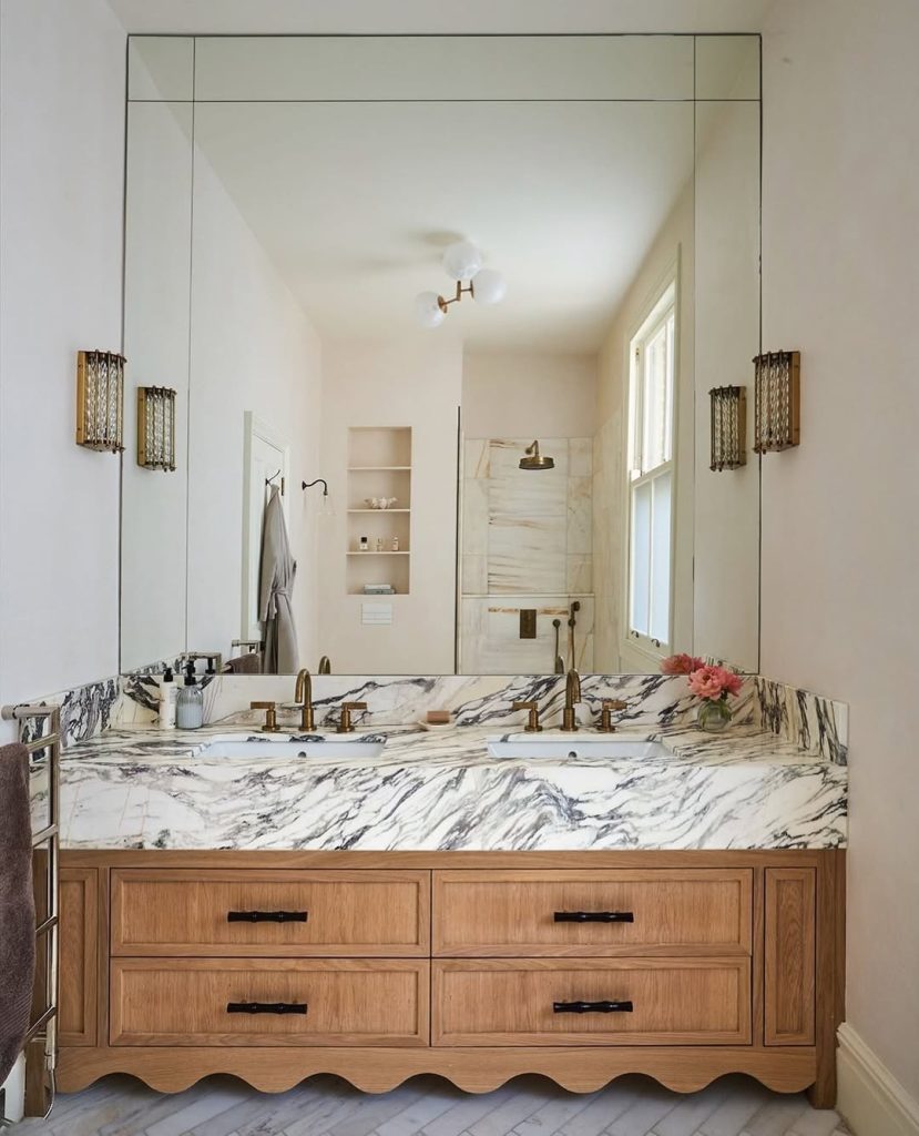 Elegant bathroom with two separate vanities featuring scalloped wood and bold marble.
