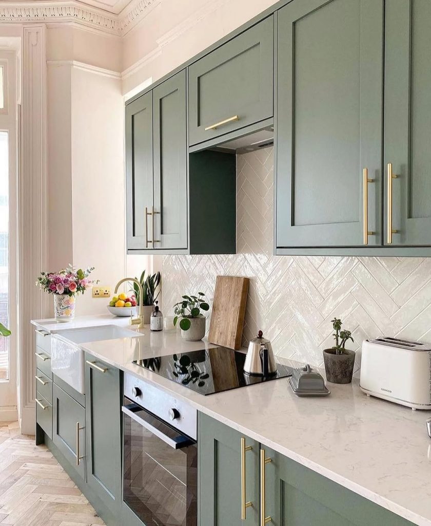 Chic green kitchen cabinets with gold handles and herringbone backsplash
